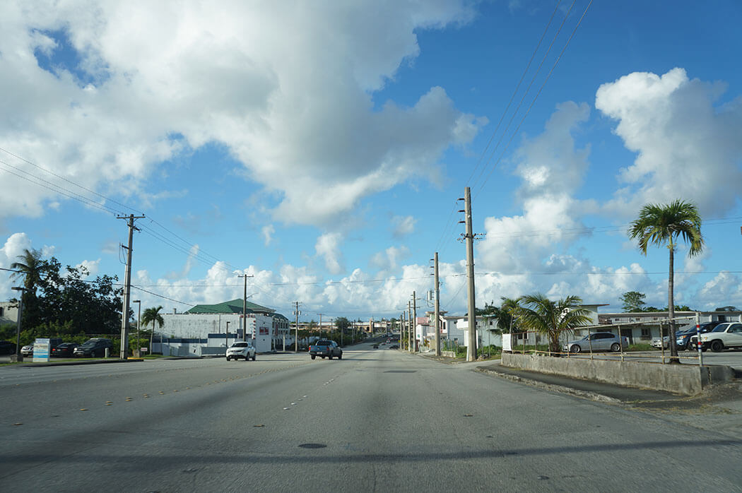 A street in Guam lined with power lines and palm trees under a cloudy sky.